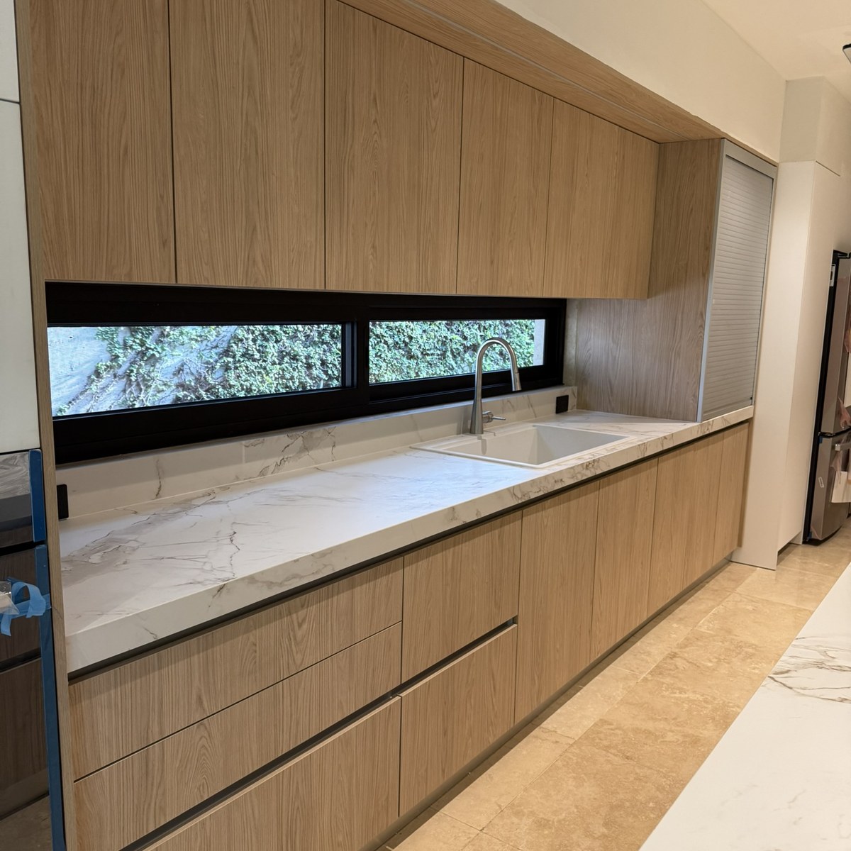 Cocina Novecci de madera clara con cubierta de piedra y ventana horizontal